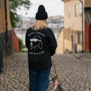 Person wearing a black hoodie with 'Anti-Social Dog Owner' text and graphic, walking a dog on a leash.