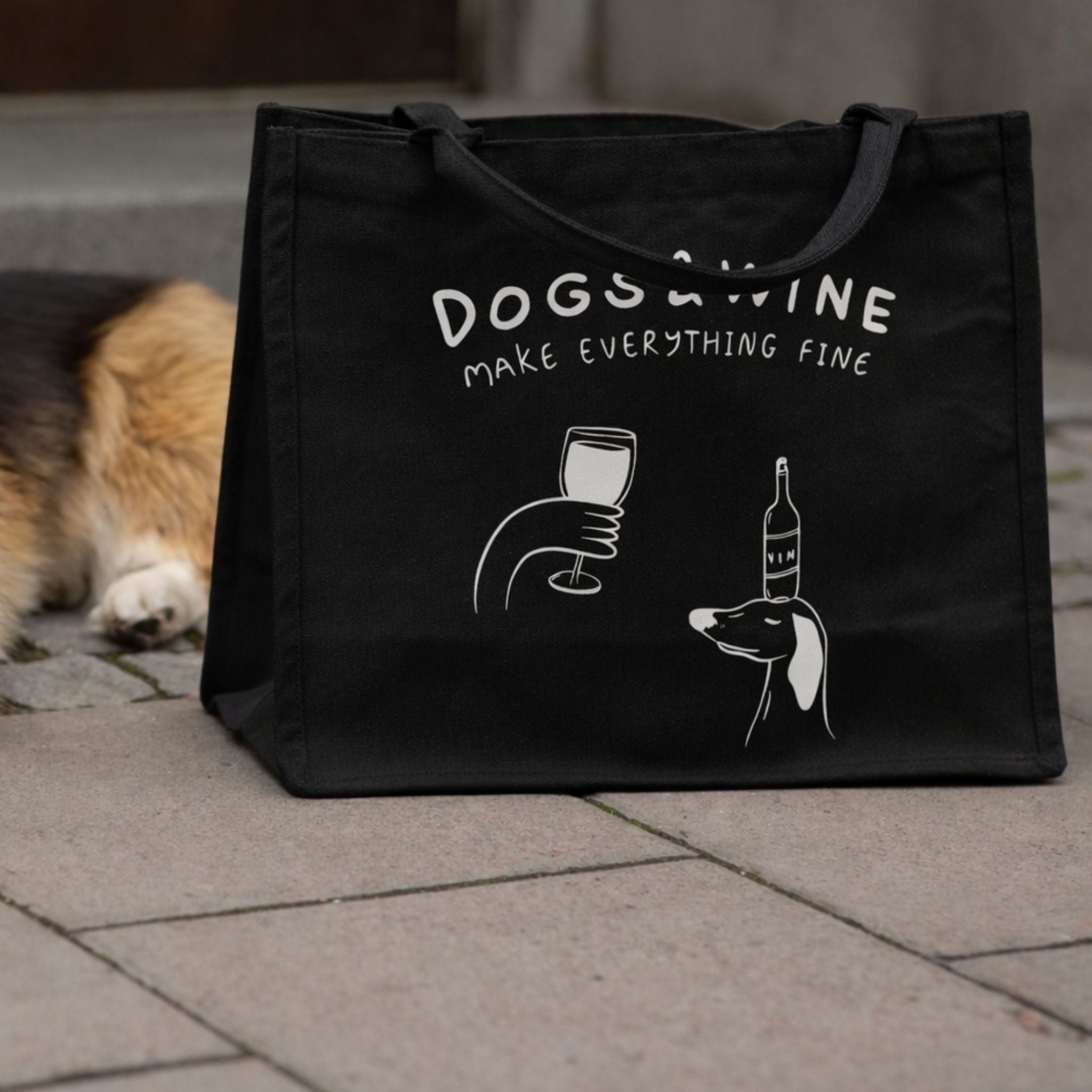 Black tote bag with 'DOGS & WINE MAKE EVERYTHING FINE' text and graphics on a stone surface.