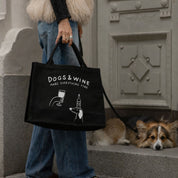Person holding a black tote bag with 'DOGS & WINE make everything fine' text and a dog lying on steps in the background.